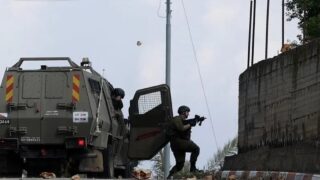 Tentara Israel membidik senjata dari samping kendaraan lapis baja di tepi jalan