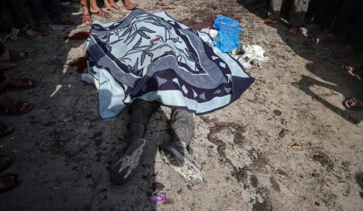Jenazah warga Palestina ditutup selimut di jalan, dikelilingi warga di Gaza.