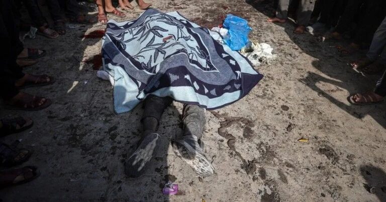 Jenazah warga Palestina ditutup selimut di jalan, dikelilingi warga di Gaza.